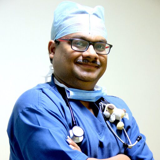 A doctor wearing scrubs and a stethoscope, smiling and standing with arms crossed.